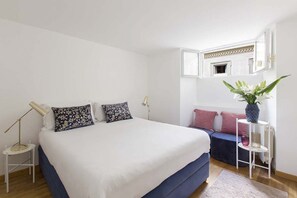Ein Schlafzimmer mit einem großen Bett, Nachttischlampen, einem kleinen Tisch, einer Bank und einer Topfpflanze.
