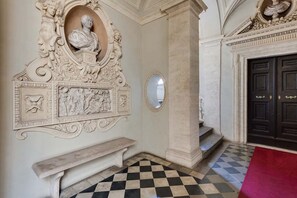 Parede de mármore com um busto, um espelho e um chão xadrez.