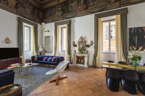 A spacious living room with a blue sofa, a white armchair, a fireplace, and a dining area with black chairs. - COSTAGUTI EXPERIENCE (Roma)