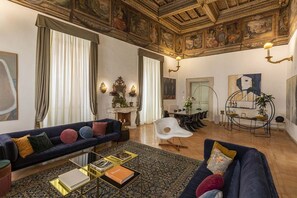 A spacious living room with a dark blue sofa, a white chair, and a coffee table with books. - COSTAGUTI EXPERIENCE (Roma)