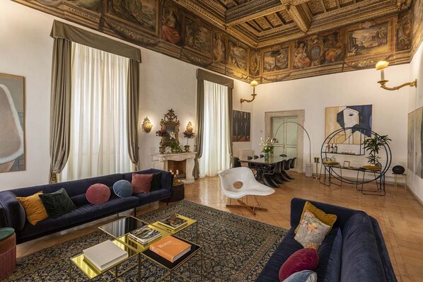 A spacious living room with a dark blue sofa, a white chair, and a coffee table with books.