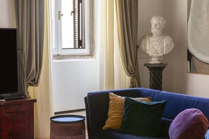 Un saló amb un sofà blau, una escultura de bust i una televisió sobre un moble de fusta.