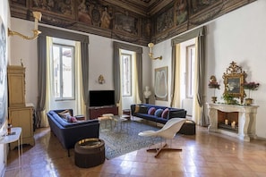 A spacious living room with a sofa, a TV, a fireplace, and a chandelier.