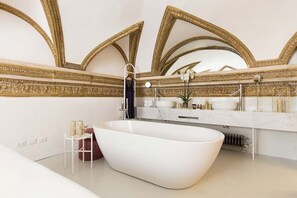 A modern bathroom with a freestanding bathtub, marble countertops, and ornate gold-framed mirrors.