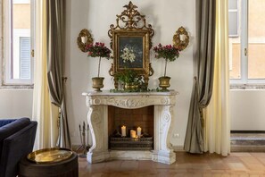 Lareira com duas velas, ladeada por dois vasos de plantas e um quadro emoldurado.
