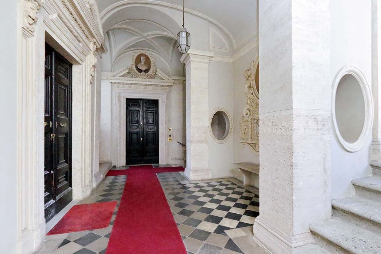 A hallway with a checkered floor, a red carpet, and a black door at the end.