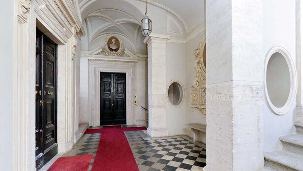Un pasillo con piso de cuadros, alfombra roja y una puerta negra al final.