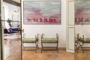 Ein Zimmer mit einem großen abstrakten Gemälde, zwei gepolsterten grünen Bänken, einem blauen Sofa und einer Topfpflanze.