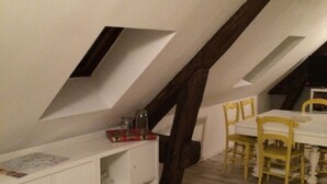A dining area with a white table and yellow chairs, a white cabinet with drawers, and a sloped ceiling with wooden beams. - The werewolf lair (Bléré)
