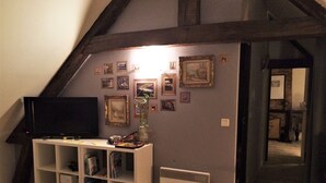 A living room with a television on a white stand, a bookshelf, and a wall decorated with framed pictures. - The werewolf lair (Bléré)