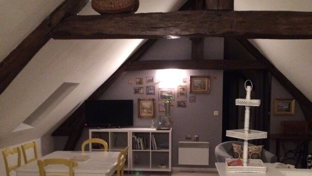 An attic dining area with a wooden table and chairs, a white cabinet, and a hanging light fixture. - The werewolf lair (Bléré)