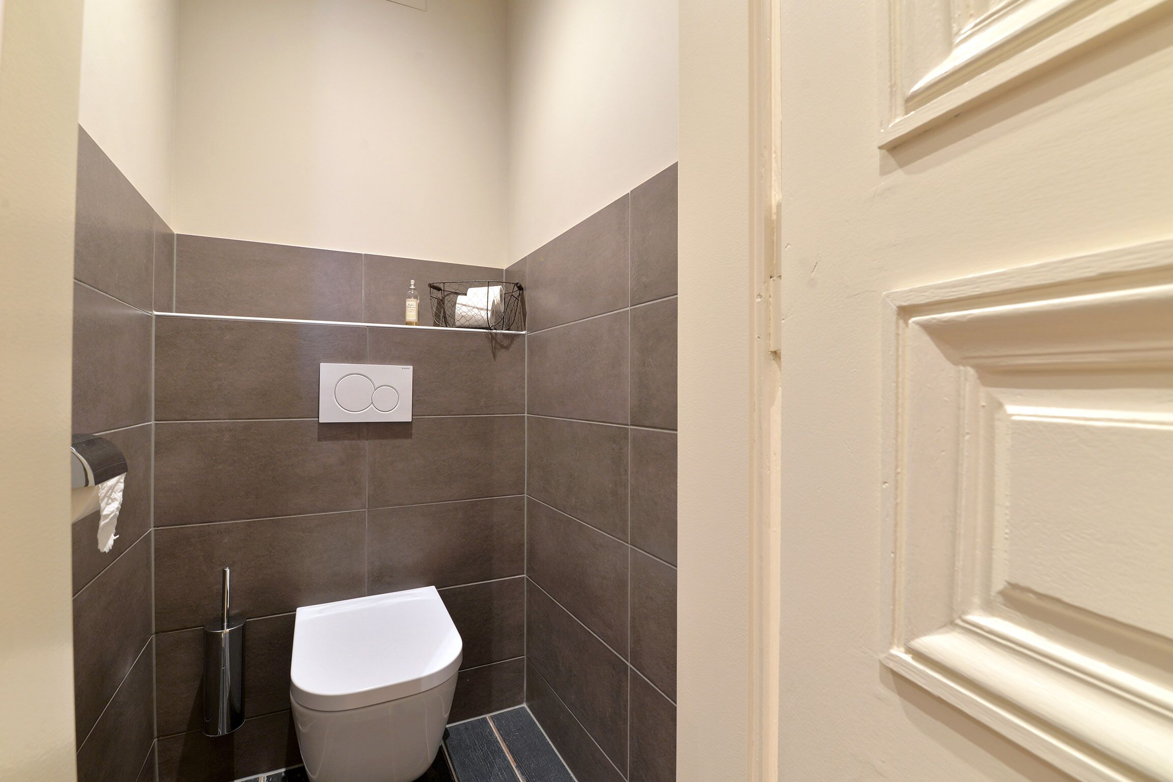 Pieni, moderni kylpyhuone, jossa on wc, käsienkuivaaja ja pyyhekoukku.