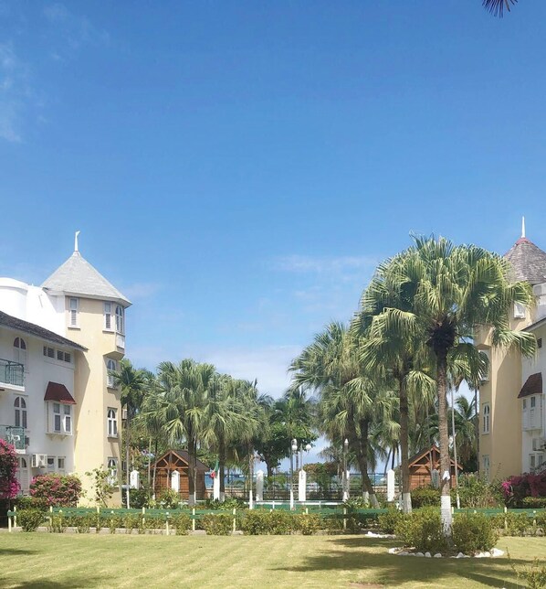 A resort with a central lawn, palm trees, and a building with a tower. - Cool's 1bd, Villa B6, On the Beach&Garden View WIFI (Ocho Rios)