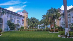 A hotel with a central lawn, palm trees, and a building with multiple balconies and a tower. - Cool's 1bd, Villa B6, On the Beach&Garden View WIFI (Ocho Rios)