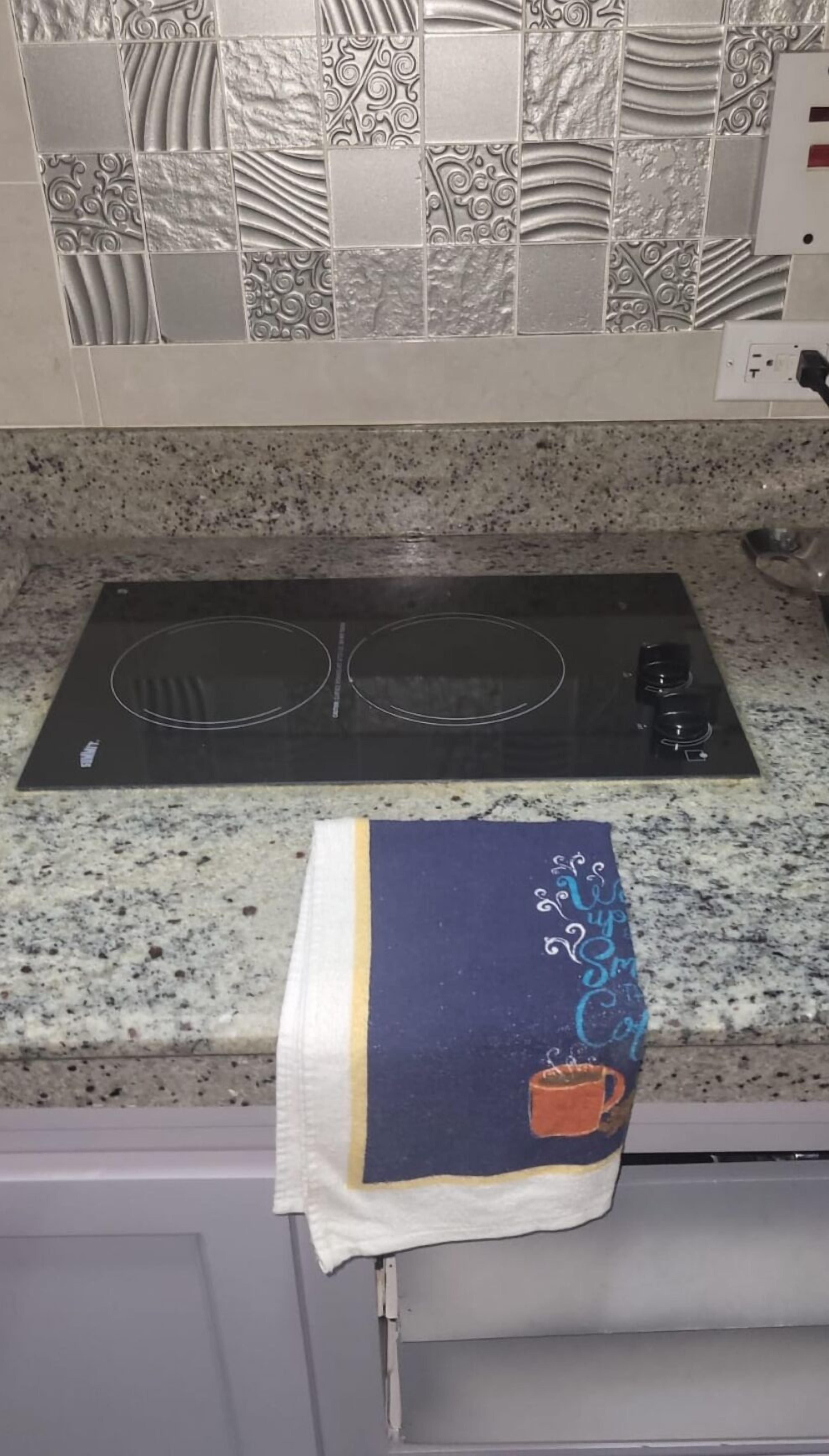 Una cocina con encimera de granito, placa de cocción por inducción negra y un salpicadero decorativo.