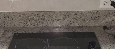 Una cocina con encimera de granito, placa de cocción por inducción negra y un salpicadero decorativo.