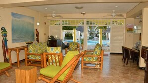A room with bamboo furniture, a painting of waves, and a view of a pool. - Cool's 1bd, Villa B6, On the Beach&Garden View WIFI (Ocho Rios)