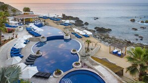 A resort with a large infinity pool, multiple lounge areas with umbrellas, and a view of the ocean.