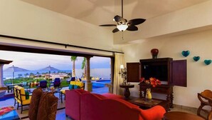 A spacious living area with a red sofa, a television, and a view of the pool and ocean.