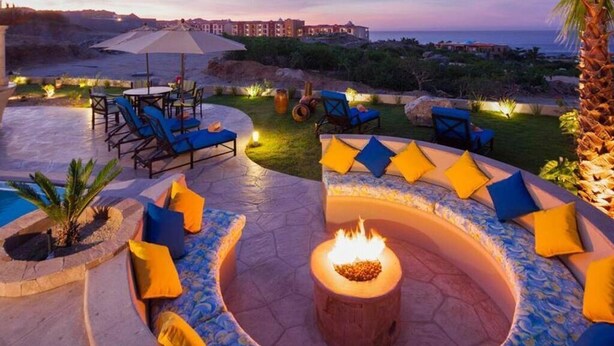 A circular outdoor seating area with a fire pit, surrounded by blue and yellow cushions.