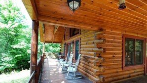 A wooden cabin with a porch, rocking chairs, and a table. - DAYBREAK LOG GETAWAY - NEW HOT TUB! (Murphy)