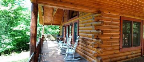 A wooden cabin with a porch, rocking chairs, and a table.