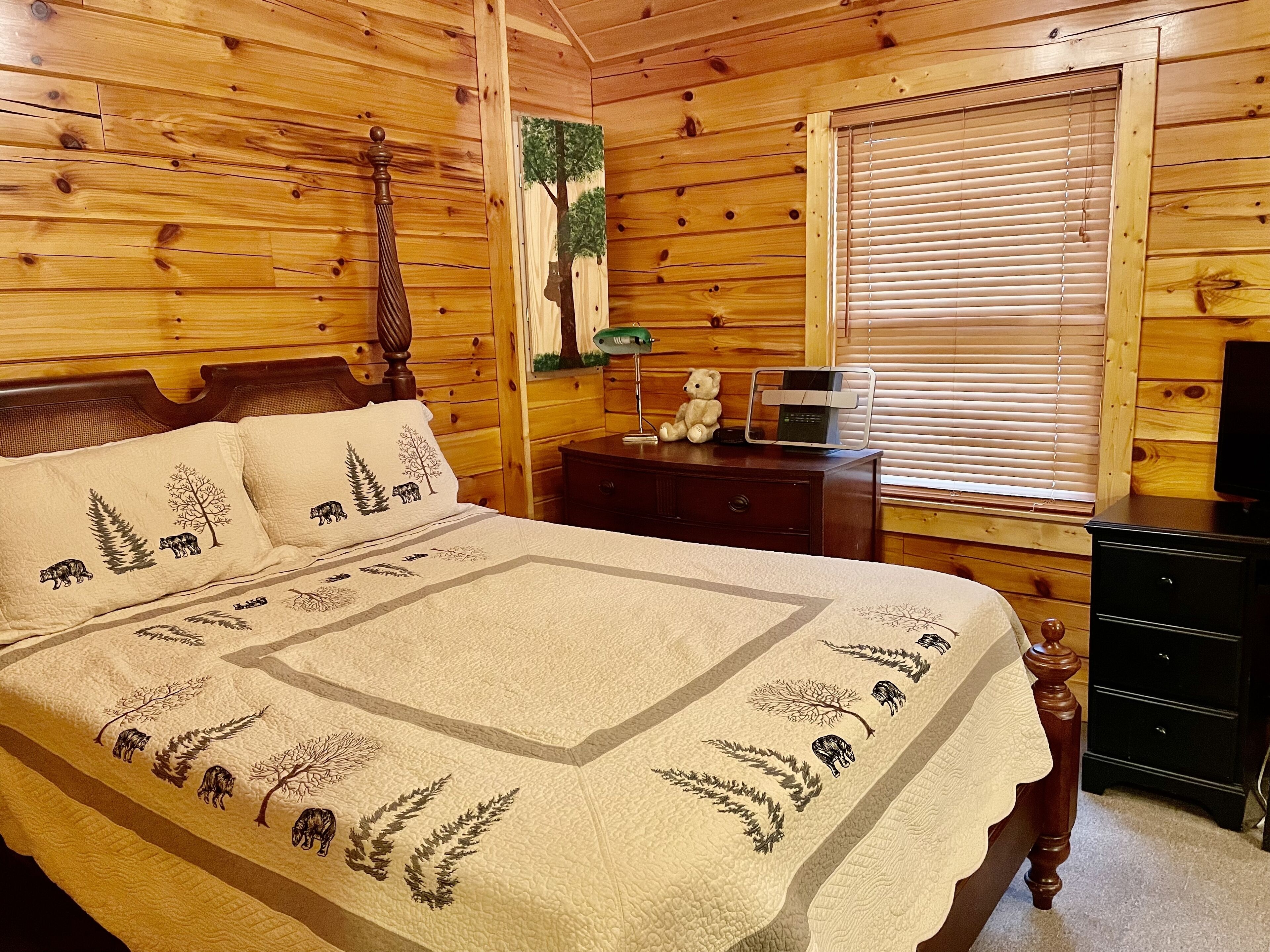 A wooden cabin bedroom with a bed, dresser, and a window with blinds.