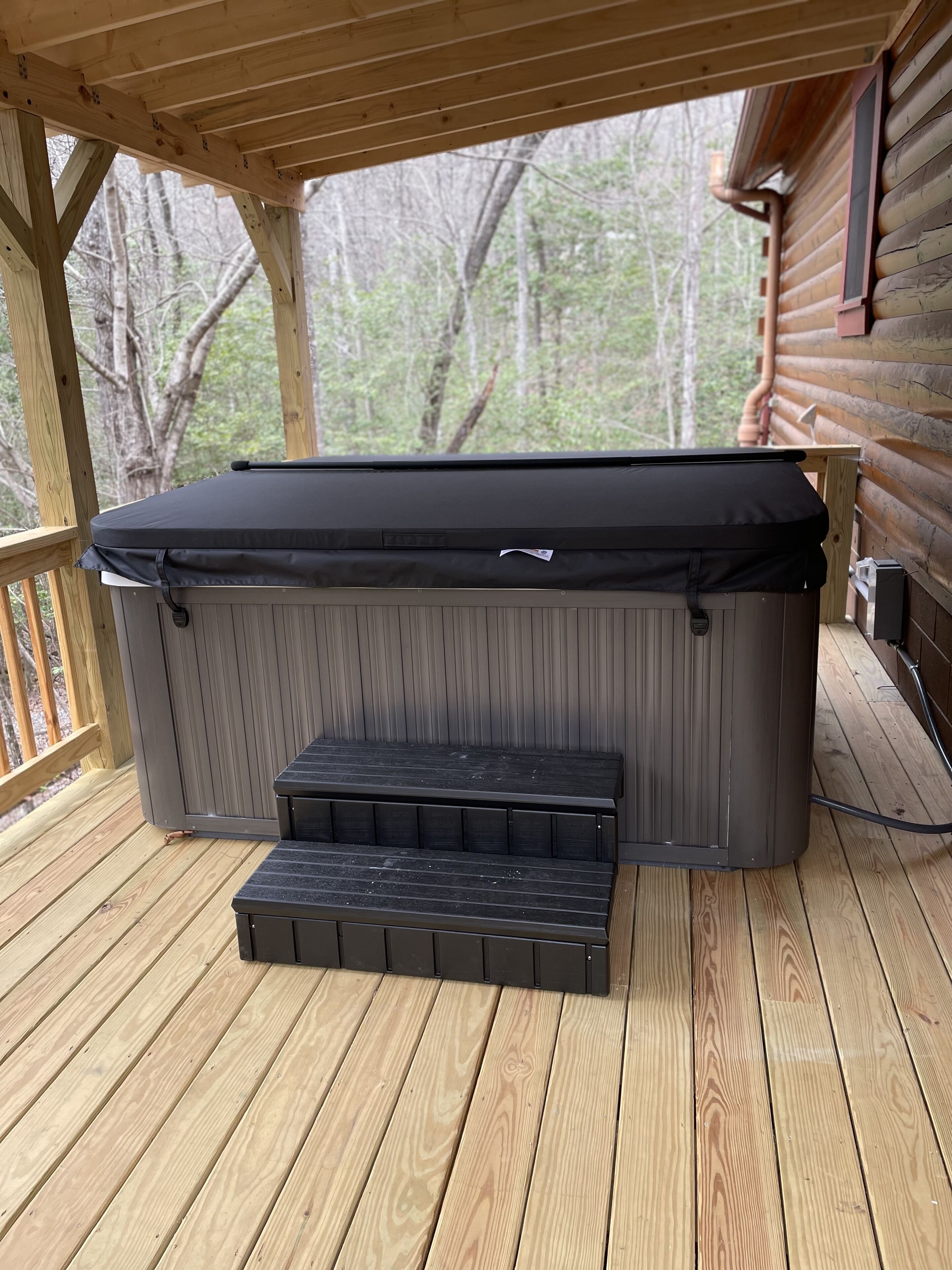 A hot tub with a black cover and a small table in front of it on a wooden deck.