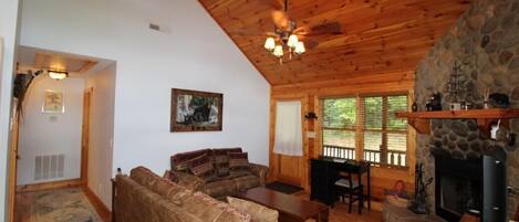 A cozy cabin interior with a stone fireplace, wooden ceiling, and a sofa set.