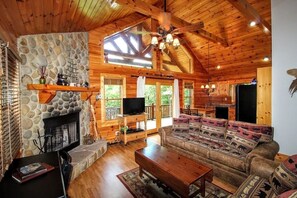 A cozy cabin interior with a stone fireplace, wooden ceiling, and a large sofa. - DAYBREAK LOG GETAWAY - NEW HOT TUB! (Murphy)
