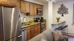 A compact kitchen with wooden cabinets, a stainless steel refrigerator, a microwave, and a coffee maker. - Location, Location! Downtown Luxury 1 Bedroom Apt (Ann Arbor)
