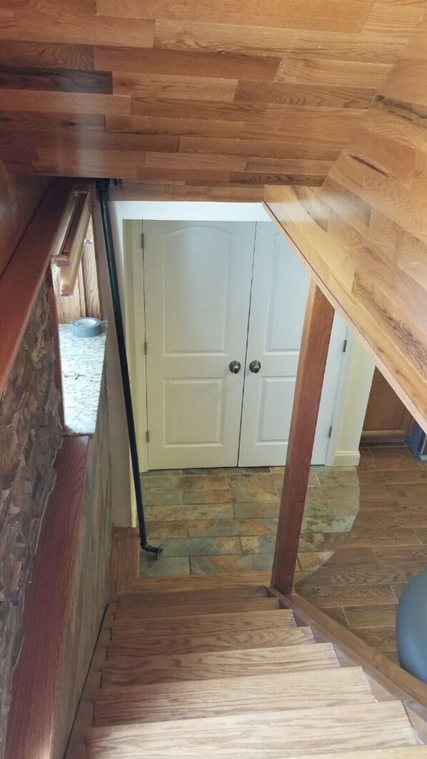 Un escalier en bois mène à une porte blanche, et le sol est recouvert de pierres.