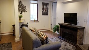 A living room with a sofa, a television, a fireplace, and a window. - Location, Location! Downtown Luxury 1 Bedroom Apt (Ann Arbor)