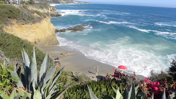 A coastal landscape with a beach, ocean waves, and a distant town.
