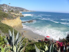 A coastal landscape with a beach, ocean waves, and a distant town.