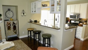 A kitchen with a central island, bar stools, a clock, and a microwave.