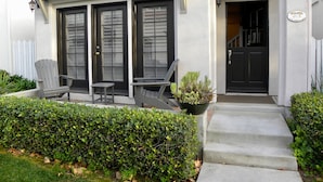 A house with a front porch, two chairs, a small table, and a potted plant.