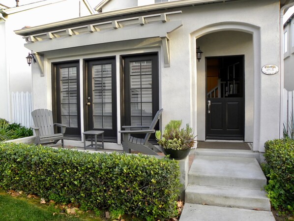 A house with a front porch, two chairs, a small table, and a potted plant.