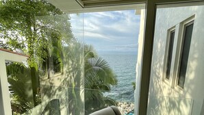 Ett rum med utsikt över havet, en fåtölj med ett mönstrat kuddöverdrag och en glasdörr som leder ut.