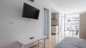 A modern bedroom with a bed, a TV mounted on the wall, a bedside table with a remote, and a door leading to a kitchen area. - Nice apartment one minute from the beach (Playa de San Juan)