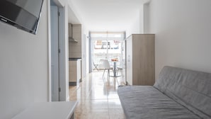 A modern living room with a grey sofa, a flat-screen TV mounted on the wall, and a kitchen area visible through an open door. - Nice apartment one minute from the beach (Playa de San Juan)