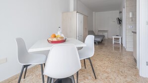 A modern, minimalist dining area with a white table and chairs, a red bowl of fruit, and a refrigerator. - Nice apartment one minute from the beach (Playa de San Juan)