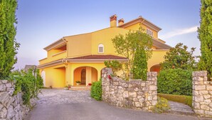 Une maison à deux étages avec une entrée surmontée d’un mur en pierre, un toit en tuiles et une petite fenêtre avec des volets.
