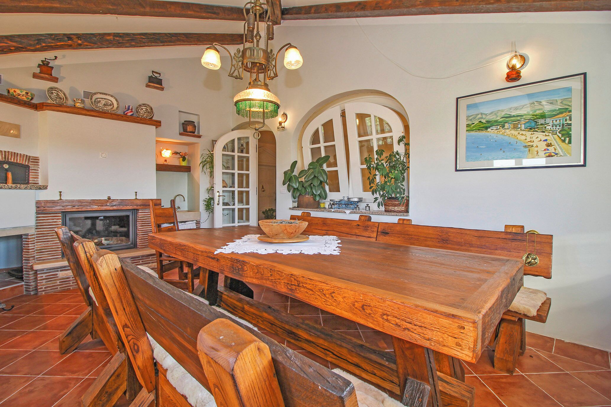 A dining area with a wooden table and benches, a fireplace, and a painting on the wall.