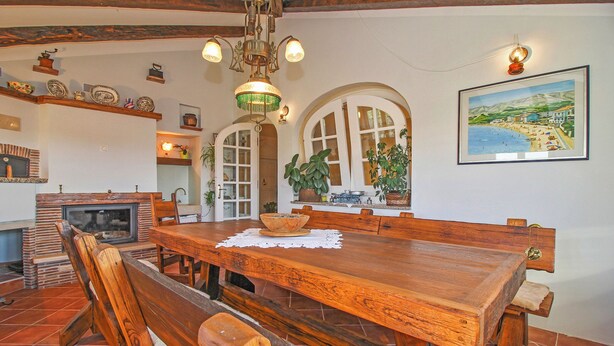 A dining area with a wooden table and benches, a fireplace, and a painting on the wall. - Leandra in Rovinjsko Selo - Istrien / Leandra in Rovinjsko Selo - Appartement für 2 Personen ST1 (Rovinj)