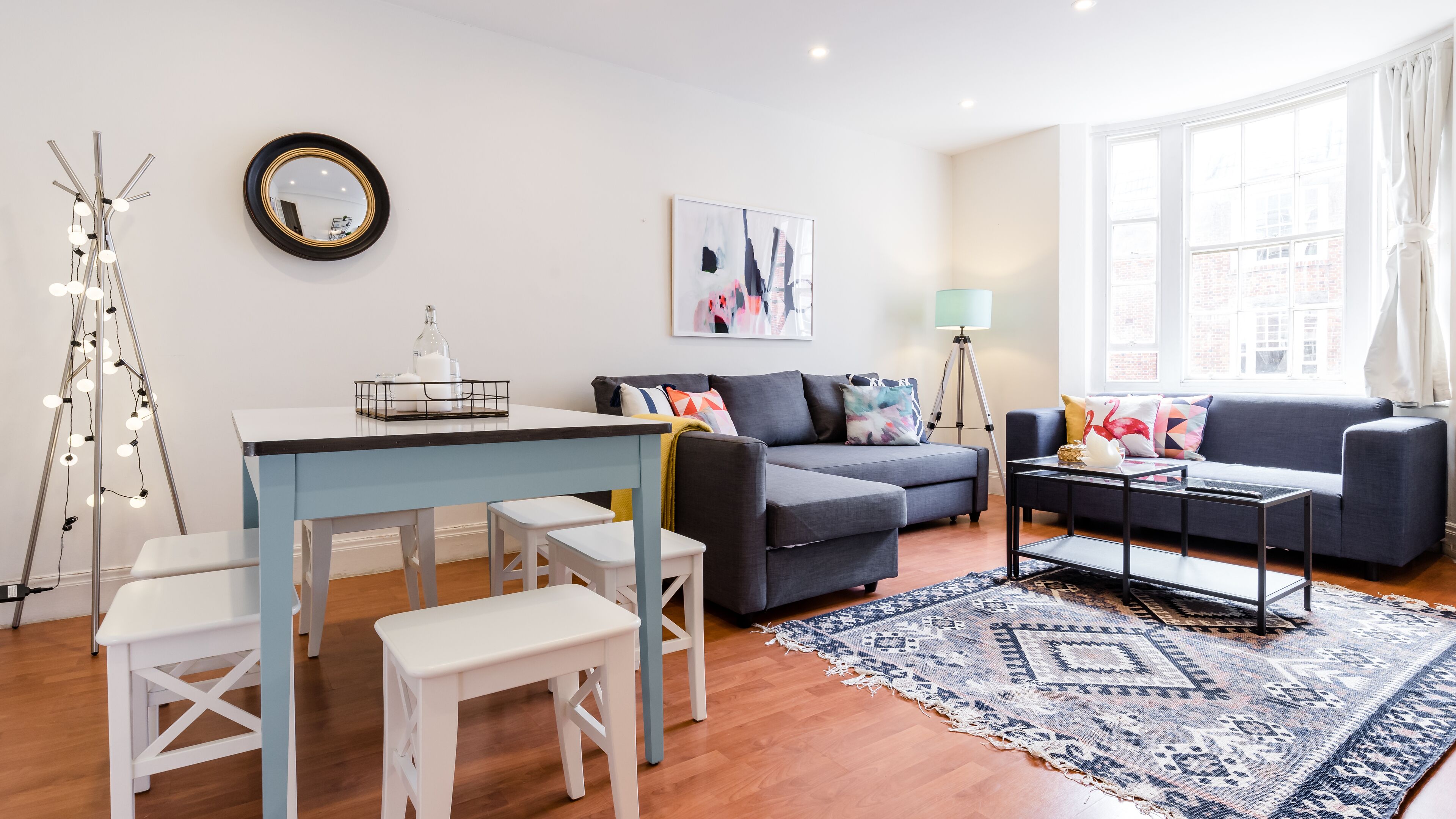 Een moderne woonkamer met een eethoek, grijze banken, een salontafel en een vloerkleed met een patroon.
