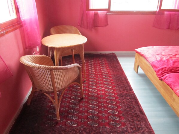Une pièce comprenant un lit, une petite table, deux chaises en osier et un tapis à motifs.