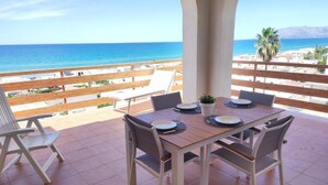 A terrace with a table set for two, overlooking a beach and mountains.
