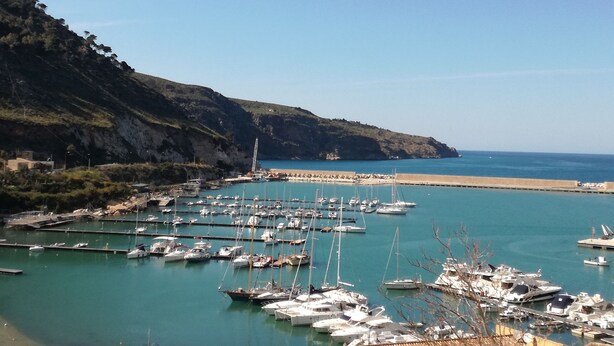 A marina with boats docked, a rocky coastline, and a clear sky.