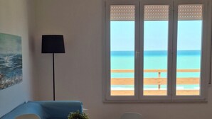 A modern room with a round dining table, white chairs, a blue sofa, a floor lamp, and a large window with a view of the beach. - Cozy and bright house with 6 beds and a panoramic terrace overlooking the sea. (Alcamo)
